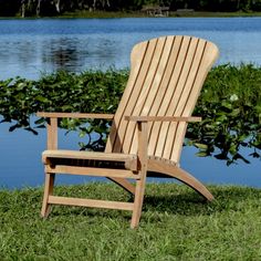 a wooden lawn chair sitting on top of a lush green field next to a lake