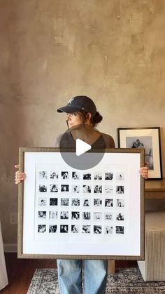 a woman holding up a framed photo in front of a wall