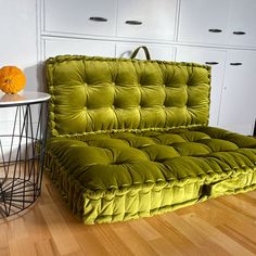 a green couch sitting on top of a hard wood floor next to a white cabinet