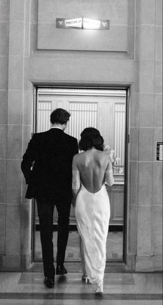 a man and woman in formal wear are walking into an elevator with their back to the camera