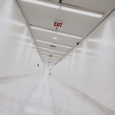 a long hallway with white walls and red exit signs on the ceiling