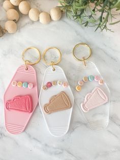 three keychains with different designs on them sitting on a marble surface next to flowers