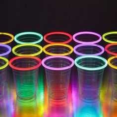 neon colored plastic cups lined up on a reflective surface with their lids open and glowing in the dark