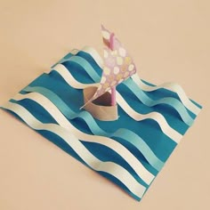 an origami boat on top of a blue and white striped paper