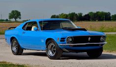 a blue muscle car parked on the side of a road in front of a field