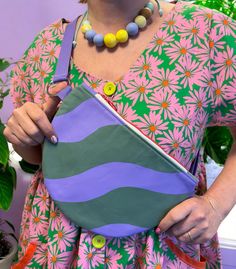 a woman is holding a purse with flowers on it and wearing a necklace that matches her dress