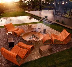 an outdoor fire pit surrounded by orange wicker chairs and tables with lights hanging from the ceiling