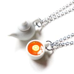 two necklaces that have food in them on a silver chain and one has a teapot with a slice of lemon