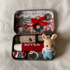 two tins with various items in them on a white tableclothed surface, one is open and the other has a red bow