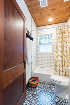 a white toilet sitting in a bathroom next to a bath tub and wooden ceilinging