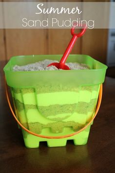 a green bucket filled with sand sitting on top of a table next to a red shovel