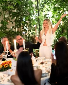 a group of people sitting around a dinner table with candles in the middle of them