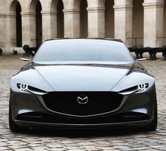 the front end of a black sports car parked on a cobblestone street with arches in the background