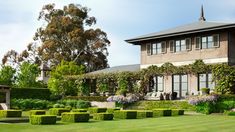 a large house surrounded by lush green grass and bushes in the foreground, with hedges on either side