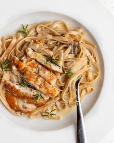 a white plate topped with pasta and chicken covered in gravy next to a fork