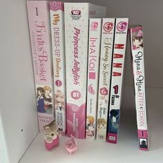 several books are stacked on top of each other in front of a white shelf with pink decorations