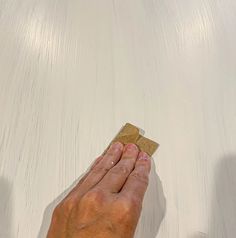 a person's hand holding a square piece of paper over a white table top