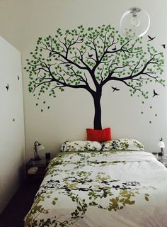 a bed room with a neatly made bed and a tree painted on the wall above it