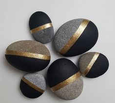 four black and gold painted rocks on a white surface