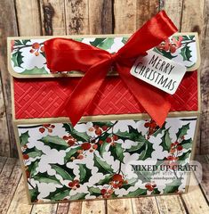 a christmas card with holly and red ribbon tied around the edge, on top of a wooden background