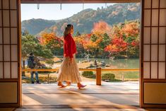 a woman standing in front of an open door looking out onto a lake and mountains