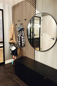 a mirror and coat hang on a wall in a room with black drawers, a bench and two coats hanging from hooks