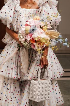 a woman in a polka dot dress holding a white purse and flowers on the runway