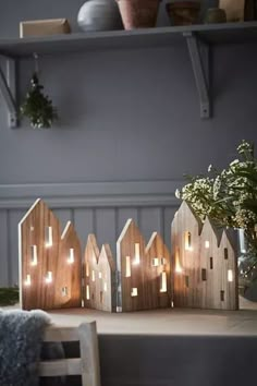 small wooden houses are lit up on a table with flowers in the vase and greenery behind them