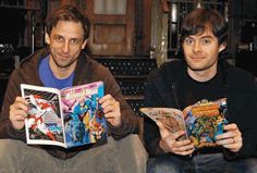 two men sitting on a bench holding comic books and looking at the same comics they are reading