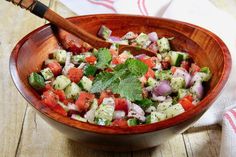 a wooden bowl filled with cucumber and red onion salad on top of a table