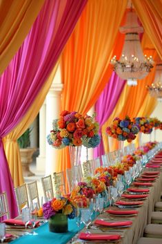 a long table is set with colorful flowers and place settings for the guests to sit down