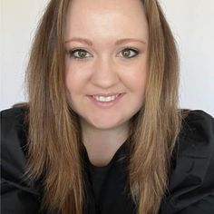 a woman with long brown hair wearing a black shirt and smiling at the camera in front of a white background