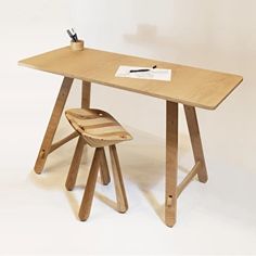 a wooden desk with a chair and pen on it, against a white background that appears to have been made out of plywood