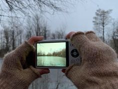 someone taking a photo with their cell phone in front of snow covered trees and water