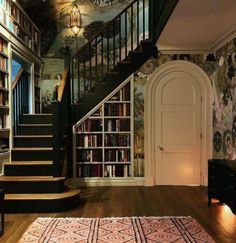 a room with stairs, bookshelves and rugs on the wooden flooring