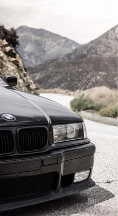 the front end of a black car parked on top of a gravel road next to mountains