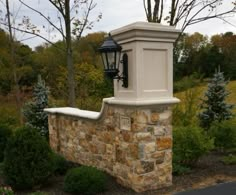 a lamp on top of a stone wall in the middle of a park with trees and bushes