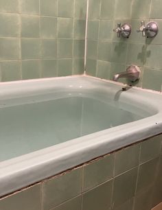 an empty bathtub in a bathroom with green tiles on the walls and flooring