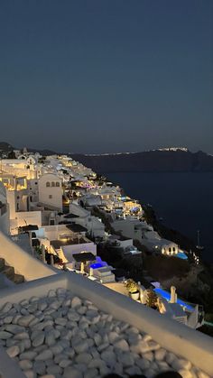 a view of the ocean and white buildings at night from atop a hill in oia