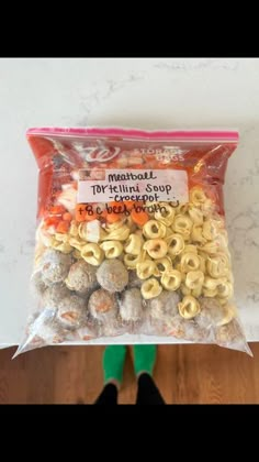 a bag of macaroni and cheese balls on top of a wooden floor next to a person's feet