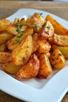 a white plate topped with fried potatoes covered in seasoning and garnished with herbs