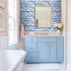 a bathroom with blue and white wallpaper, gold framed mirror, pink rug, and bathtub