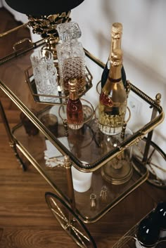 two bottles of champagne are sitting on a bar cart with glasses and wine bottle holders