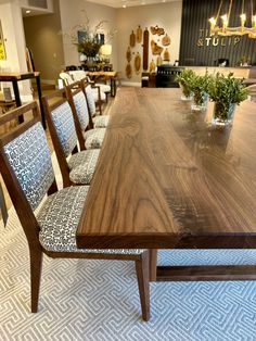 a dining room table with chairs and vases on the top, in front of an open floor plan