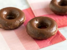 two chocolate donuts sitting on top of a pink and white checkered table cloth