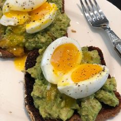 two pieces of bread with an egg and avocado on it, along with a fork