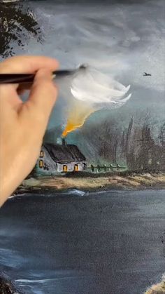 a person is holding a paintbrush in their hand and painting a house on the water