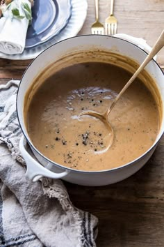 a white bowl filled with soup on top of a wooden table next to silverware