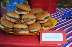 a plate full of pulled pork sliders on a red and blue table cloth with a sign