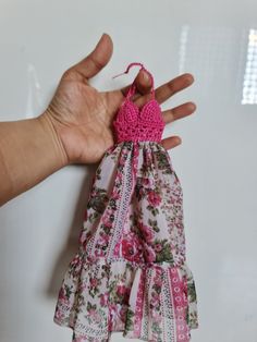 a hand is holding a small doll in a dress